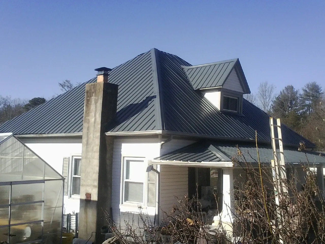 Dark blue standing seam metal roof on a white farmhouse with dormer — Slate & Tile Roof Repair by Roofing Brothers in Golf