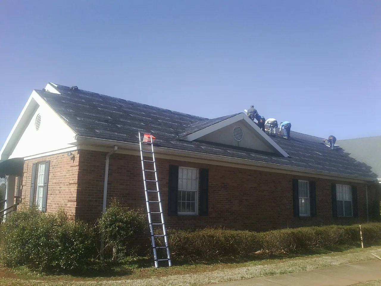 Crew tearing shingles off a brick ranch roof with a ladder set — Metal Roof Repair work by our crew in Golf