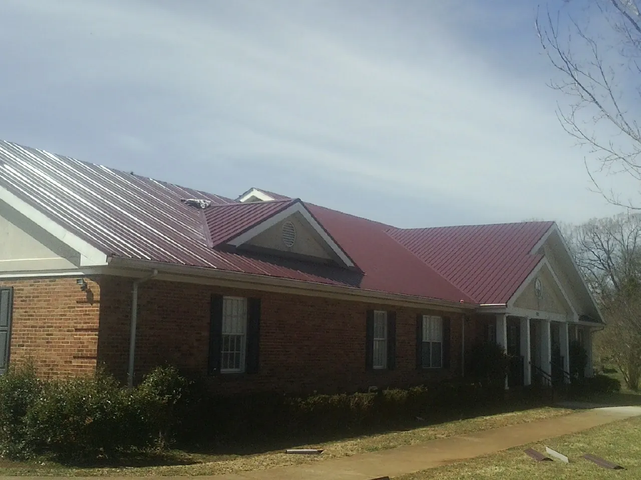 Red metal roof with gabled entries on a long brick building, from a Hail Damage Roof Repair job in Golf