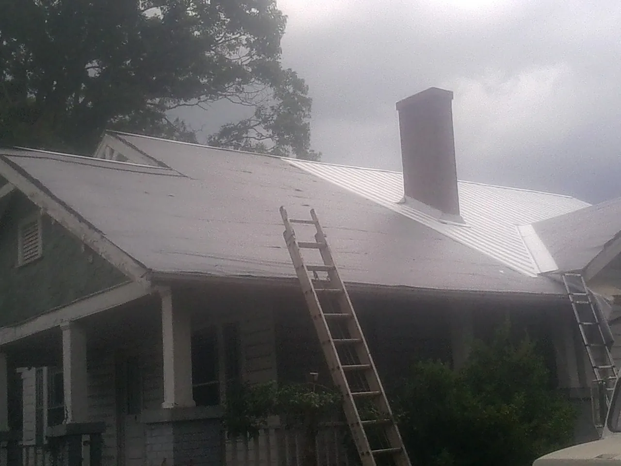 Ladders against a metal roof on an older home with a brick chimney in Golf