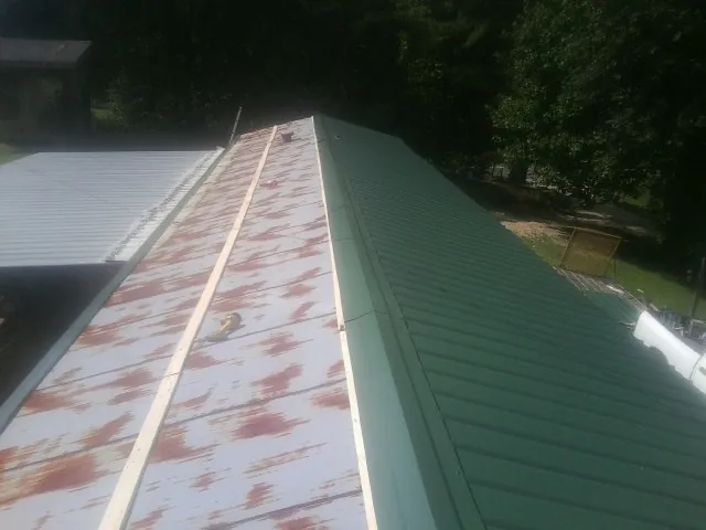 Old rusted panels beside newly installed green metal roofing — Wind Damage Roof Repair by Roofing Brothers in Golf