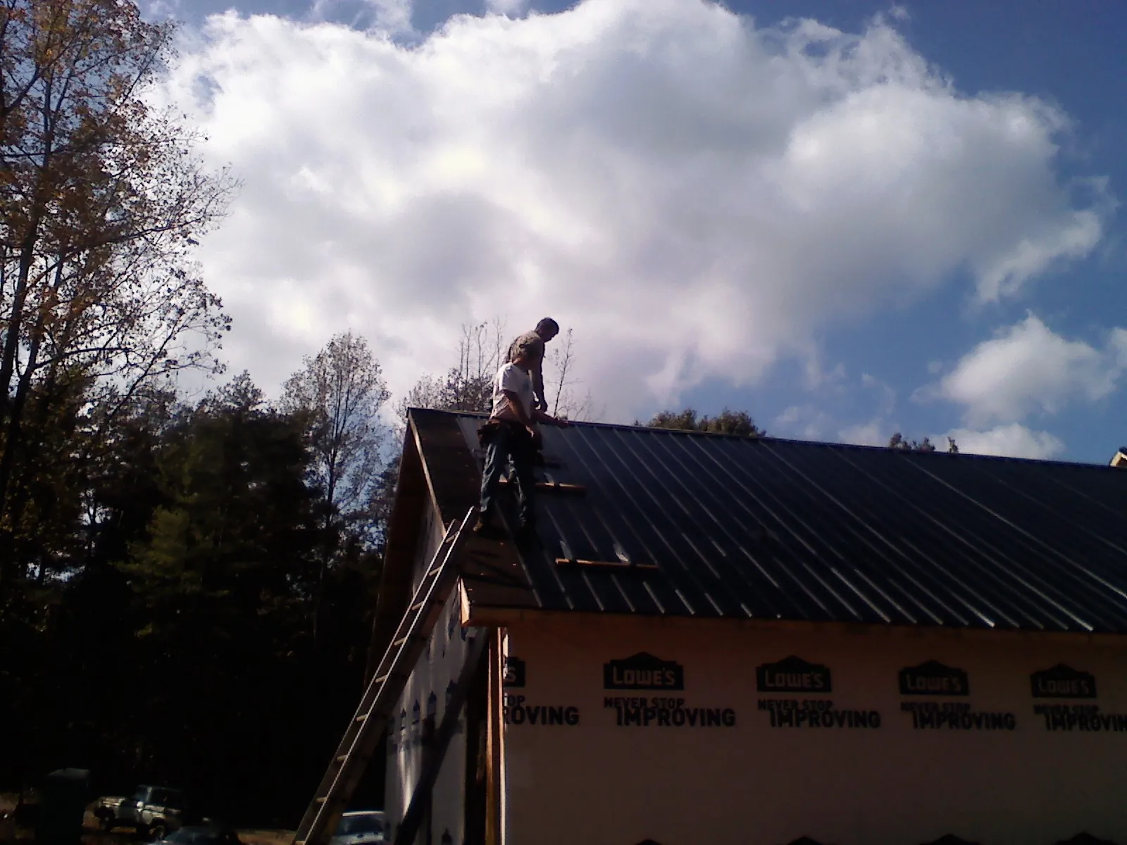 Roofer fastening dark metal panels high against a cloudy sky, from a Roof Inspection job in Golf