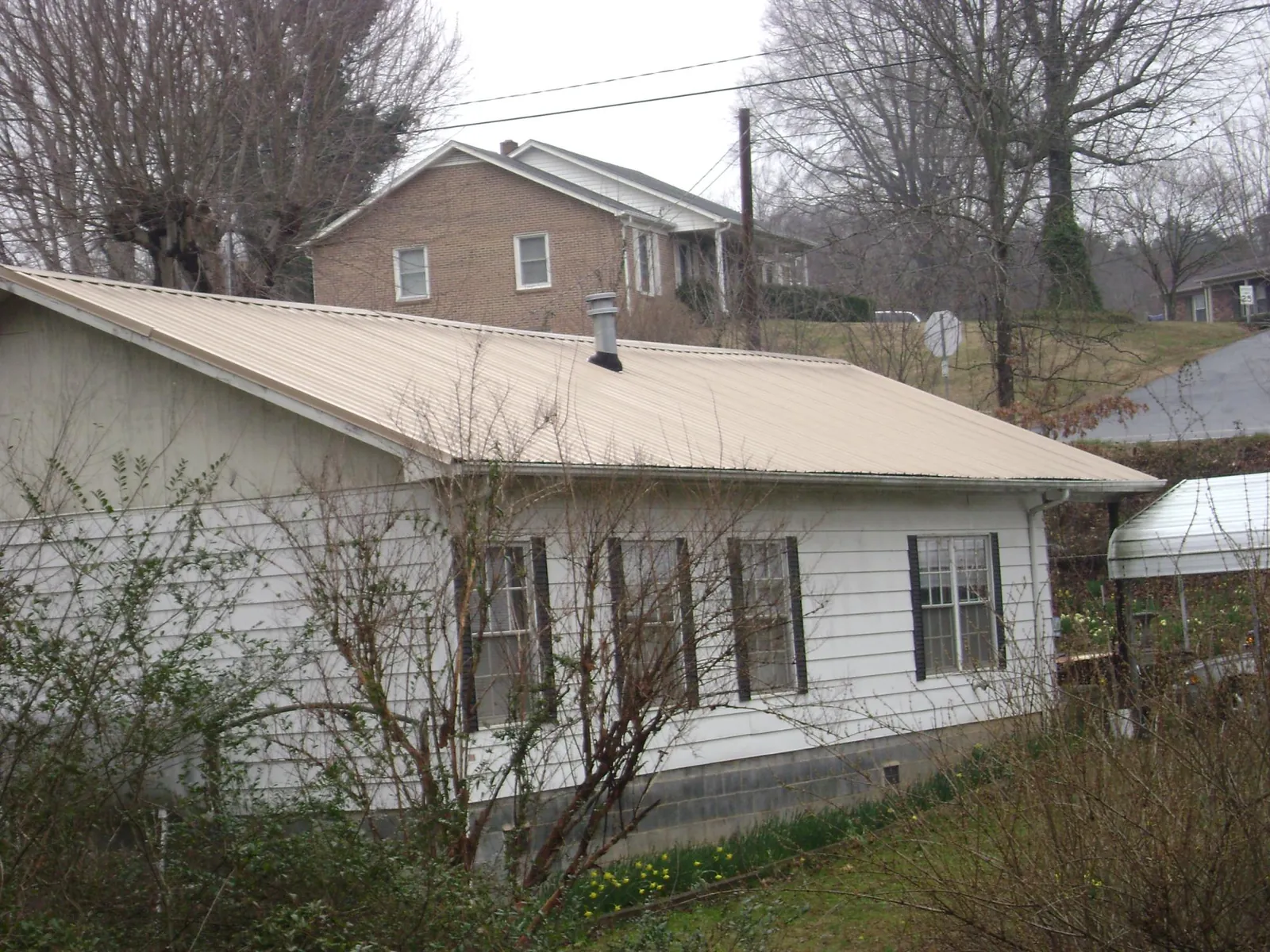 Tan metal roof on a white sided house set into a hillside — Commercial Roofing by Roofing Brothers in Golf