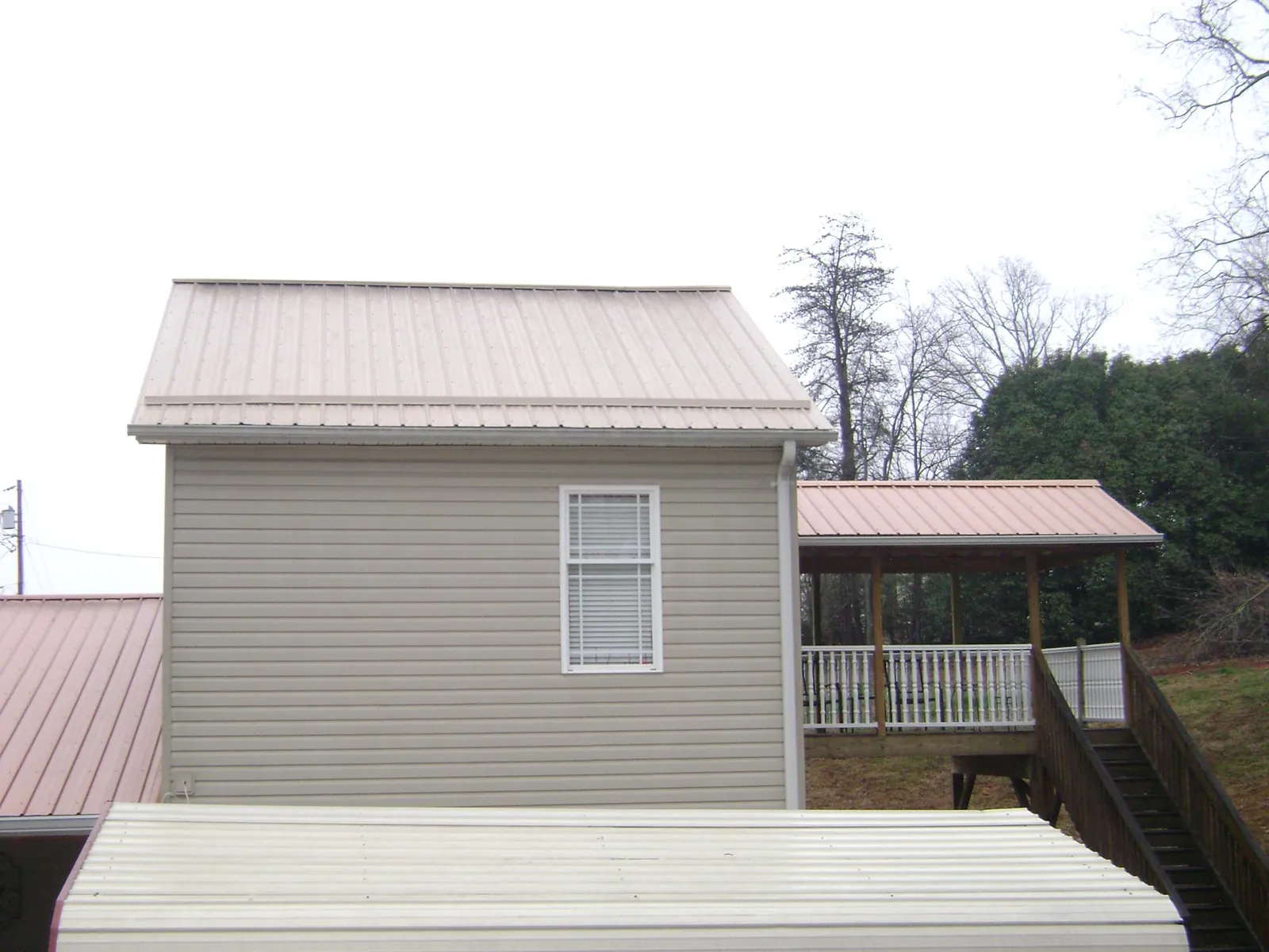Tan metal roofs on a two story addition and attached porch, from a Roof Replacement job in Golf